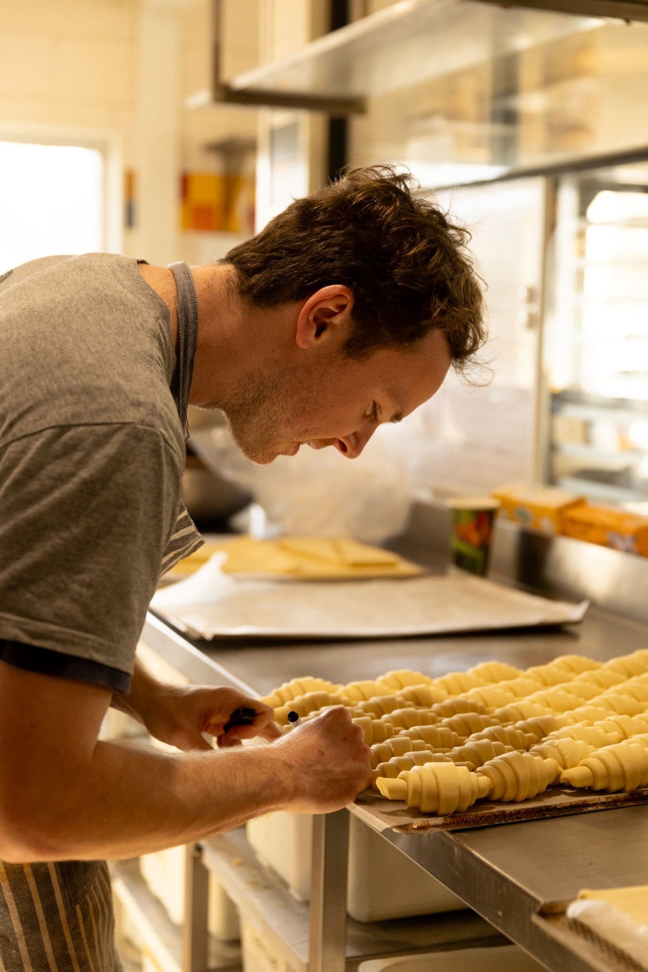 A baker checking trays of shaped croissants before baking